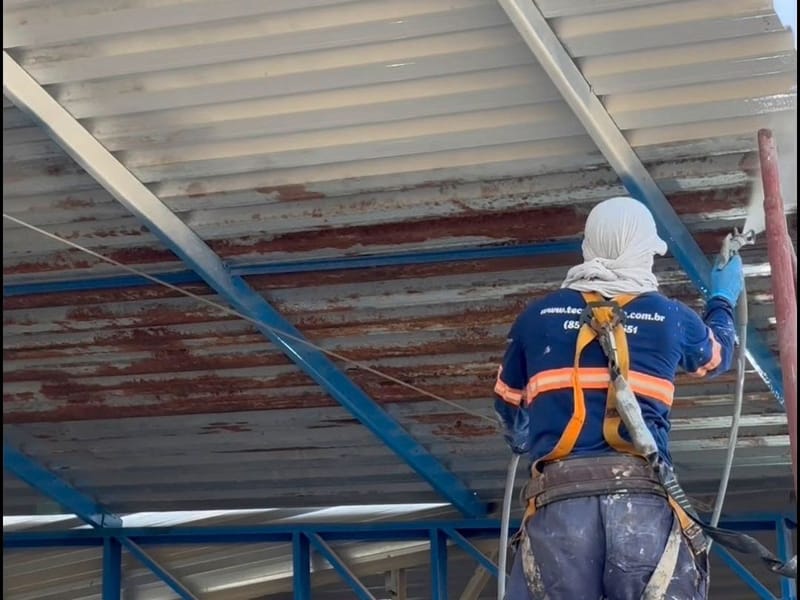 Aplicador em andaime pintando de branco a cobertura metálica enferrujada de um galpão