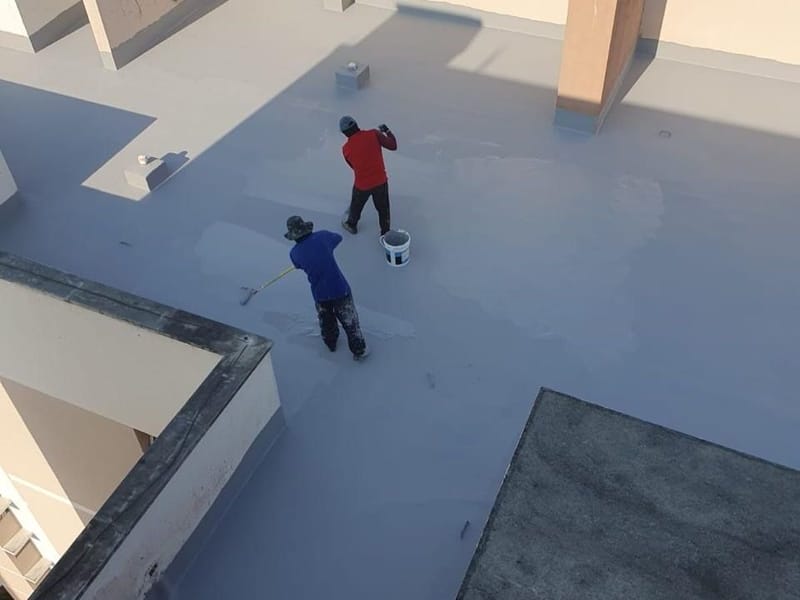 Dois aplicadores impermeabilizando a laje de cobertura de um prédio