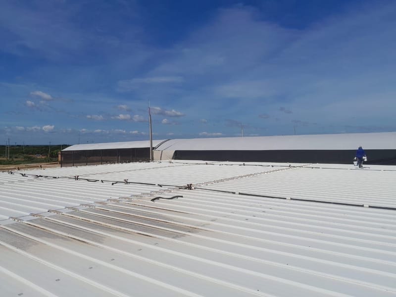 Telhado metálico de grande extensão sob sol forte e céu de nuvens